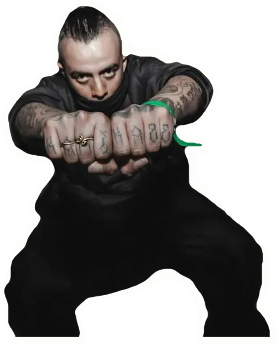 DJ KM1KC, accroupi, tend ses poings tatoués vers l’objectif.