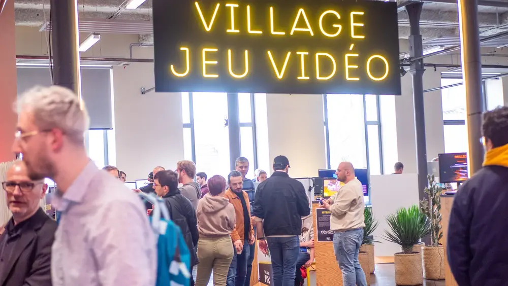 L’enseigne lumineuse « Village jeu vidéo » au-dessus des visiteurs, dans la halle de l’Imaginarium.