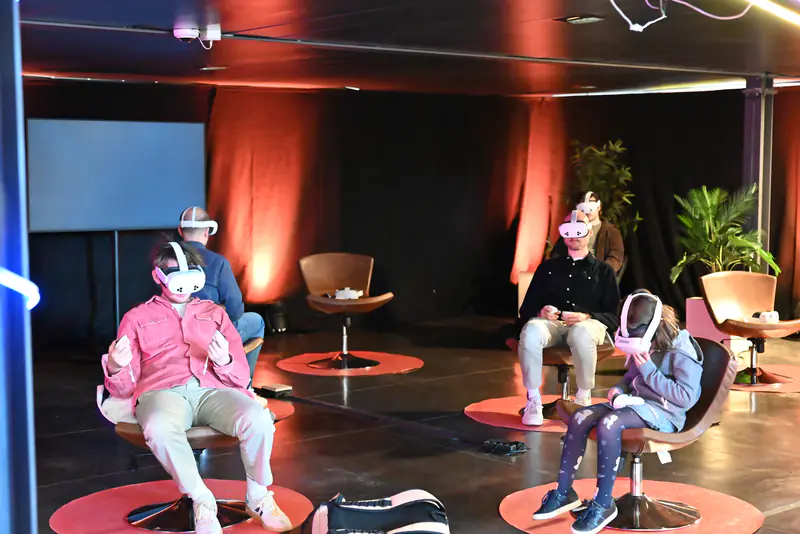 Le village VR : des visiteurs assis dans des fauteuils pivotants, casque de réalité virtuelle sur les yeux.